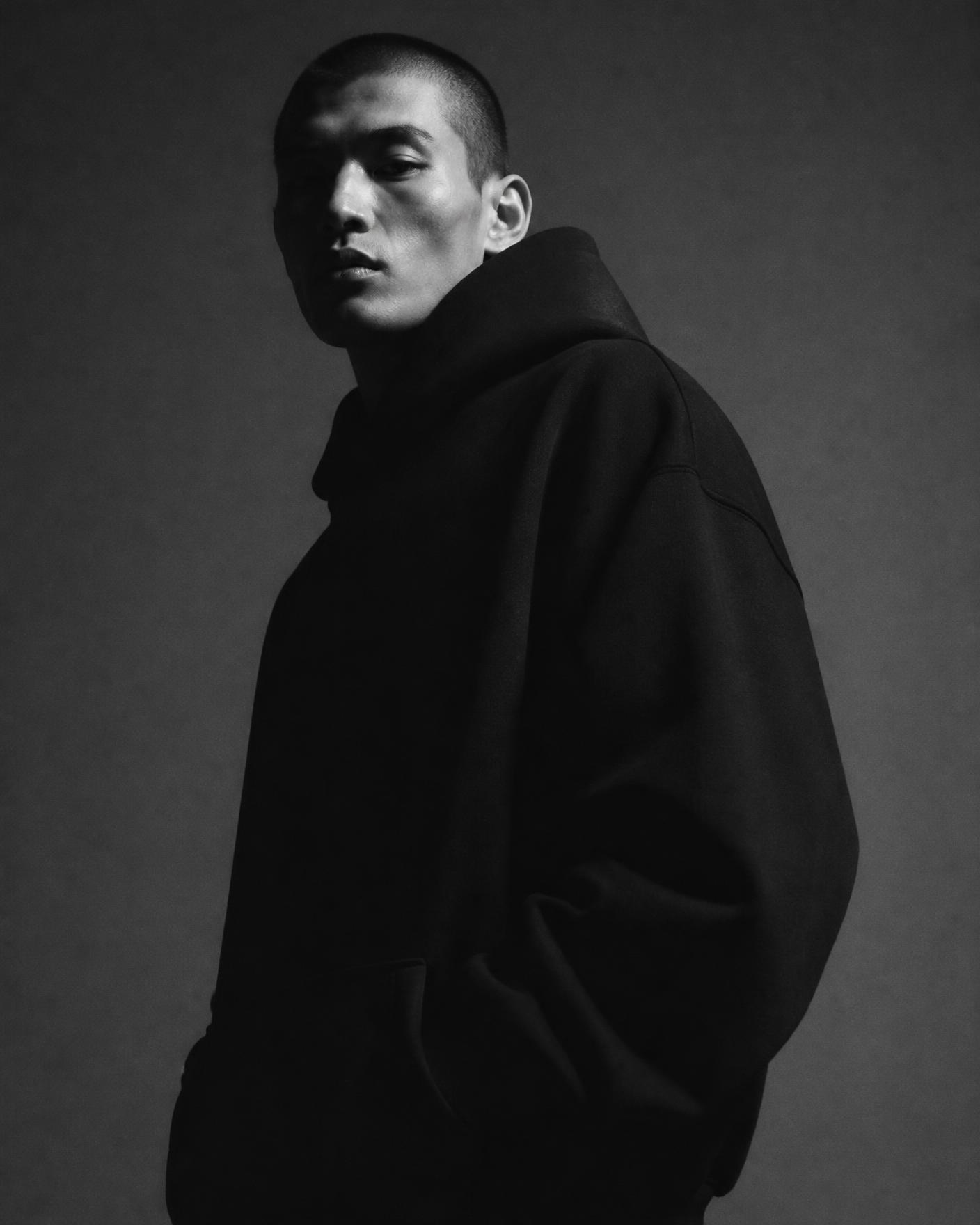 Model wearing an oversized heavyweight black hoodie against a charcoal studio backdrop